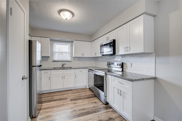 kitchen featuring white cabinetry, sink, dark stone countertops, stainless steel appliances, and light wood-type flooring