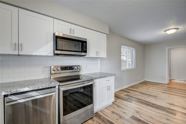 kitchen with stainless steel appliances, light stone countertops, light wood-type flooring, and white cabinets