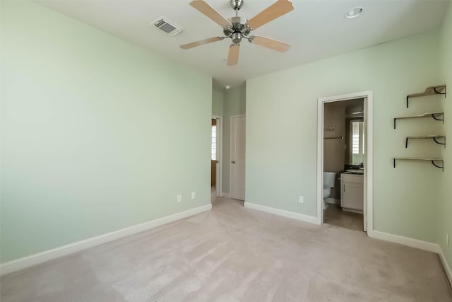 unfurnished bedroom with multiple windows, ensuite bathroom, light carpet, and ceiling fan