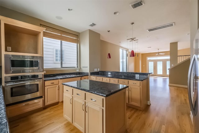 kitchen with appliances with stainless steel finishes, decorative light fixtures, dark stone countertops, a center island, and light hardwood / wood-style floors