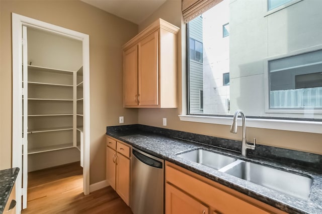 kitchen featuring light brown cabinetry, sink, dark stone counters, stainless steel dishwasher, and light hardwood / wood-style flooring