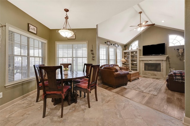 dining room featuring ceiling fan, a healthy amount of sunlight, vaulted ceiling, and a tile fireplace