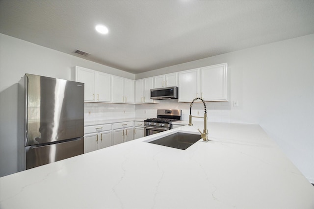 kitchen with white cabinetry, backsplash, light stone counters, and stainless steel appliances