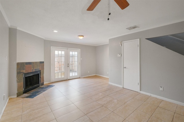 unfurnished living room featuring french doors, light tile patterned flooring, crown molding, ceiling fan, and a tiled fireplace