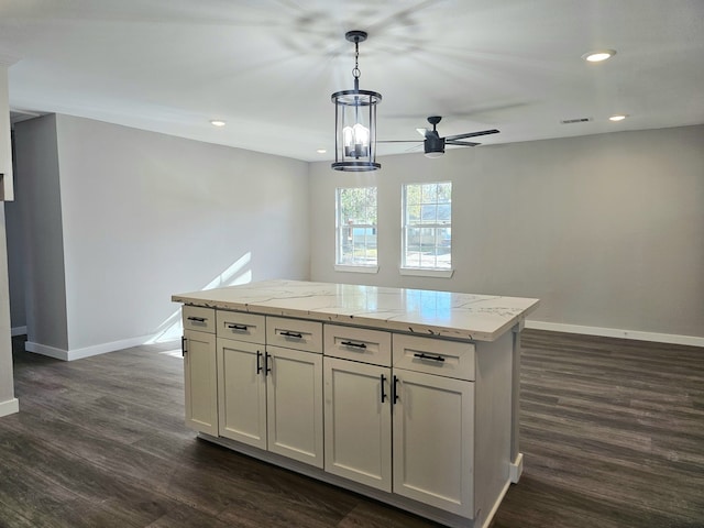 kitchen with light stone counters, decorative light fixtures, a center island, dark hardwood / wood-style floors, and ceiling fan