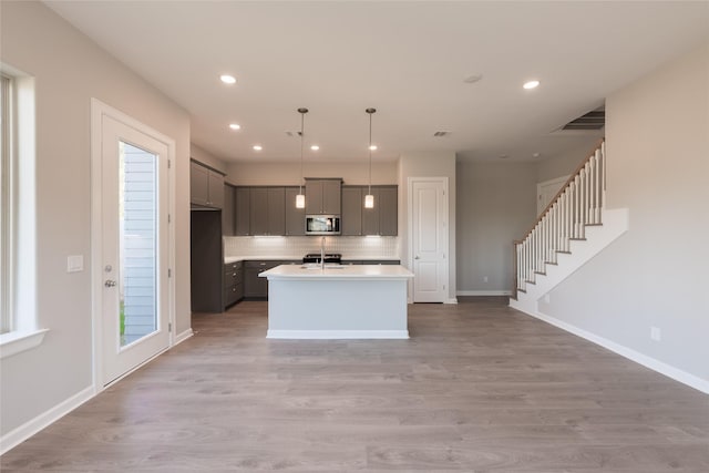 kitchen with a kitchen island with sink, decorative light fixtures, tasteful backsplash, and light wood-type flooring