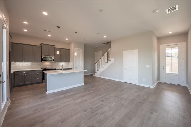 kitchen with gray cabinetry, tasteful backsplash, wood-type flooring, an island with sink, and pendant lighting