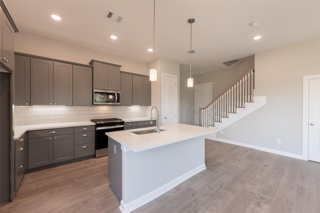 kitchen featuring pendant lighting, an island with sink, sink, gray cabinetry, and stainless steel appliances