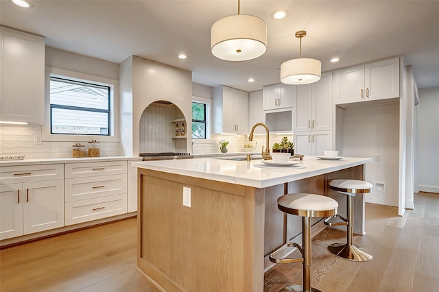 kitchen featuring decorative light fixtures, white cabinetry, sink, a kitchen island with sink, and light hardwood / wood-style floors