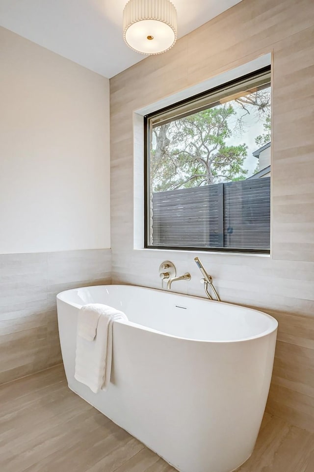 bathroom featuring plenty of natural light, tile walls, and a tub