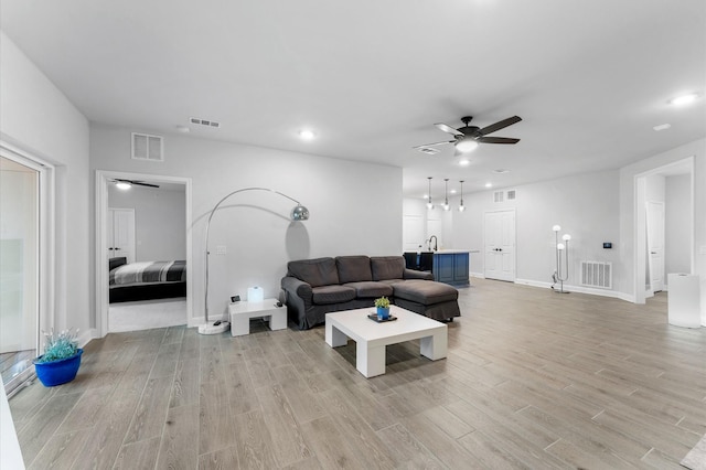 living room featuring ceiling fan, sink, and light wood-type flooring