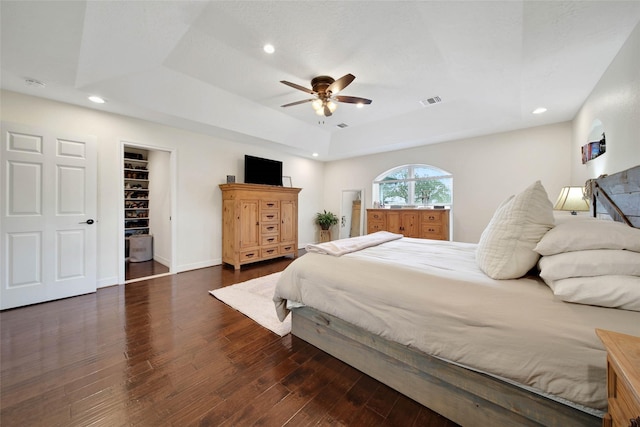 bedroom featuring ceiling fan, a tray ceiling, dark hardwood / wood-style flooring, and a spacious closet