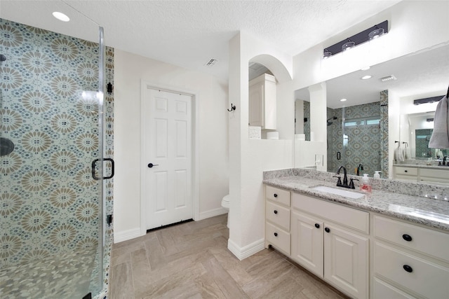 bathroom featuring a shower with door, vanity, a textured ceiling, and toilet