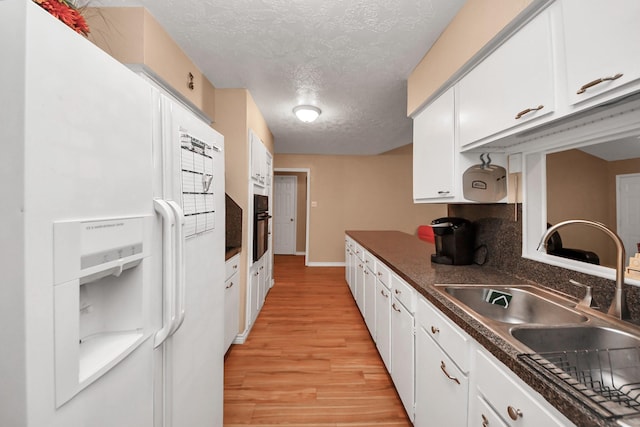 kitchen featuring sink, black oven, white refrigerator with ice dispenser, white cabinets, and light wood-type flooring