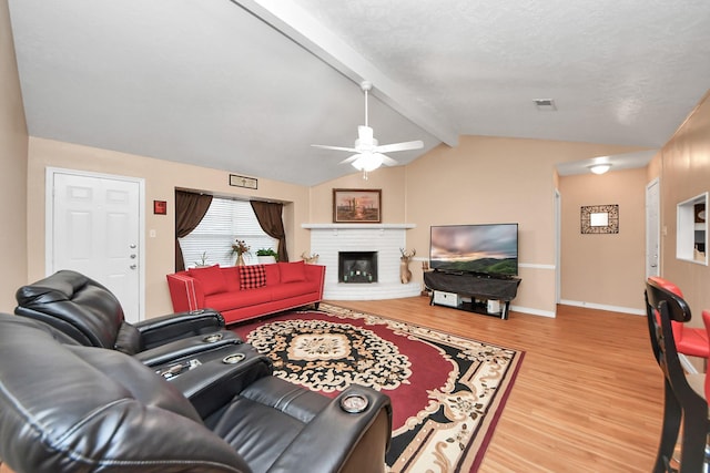 living room with a brick fireplace, light hardwood / wood-style flooring, lofted ceiling with beams, and ceiling fan