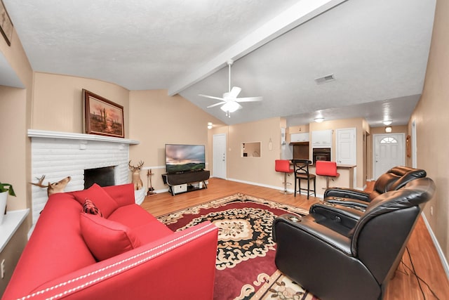 living room featuring lofted ceiling with beams, a textured ceiling, hardwood / wood-style flooring, ceiling fan, and a fireplace