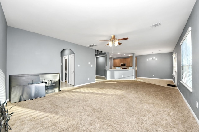 unfurnished living room with ceiling fan with notable chandelier and light colored carpet