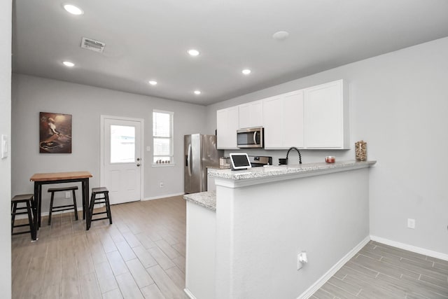 kitchen with sink, light stone counters, appliances with stainless steel finishes, kitchen peninsula, and white cabinets