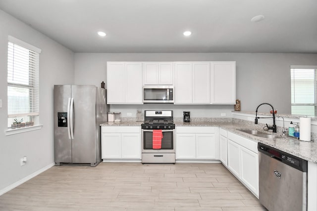 kitchen with appliances with stainless steel finishes, sink, white cabinets, light stone countertops, and light wood-type flooring