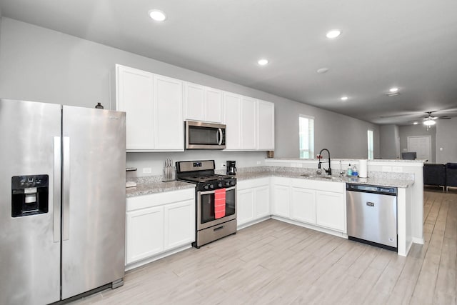 kitchen with sink, stainless steel appliances, light stone counters, light hardwood / wood-style floors, and white cabinets