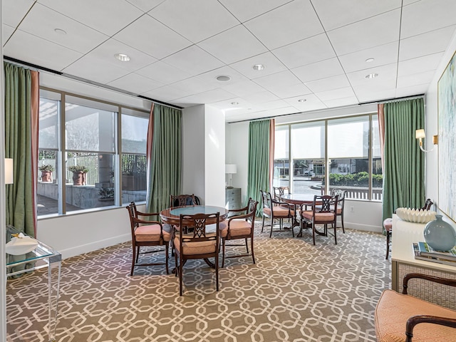 carpeted dining space with a water view and a paneled ceiling