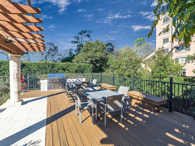 wooden deck with a grill, a pergola, and an outdoor kitchen