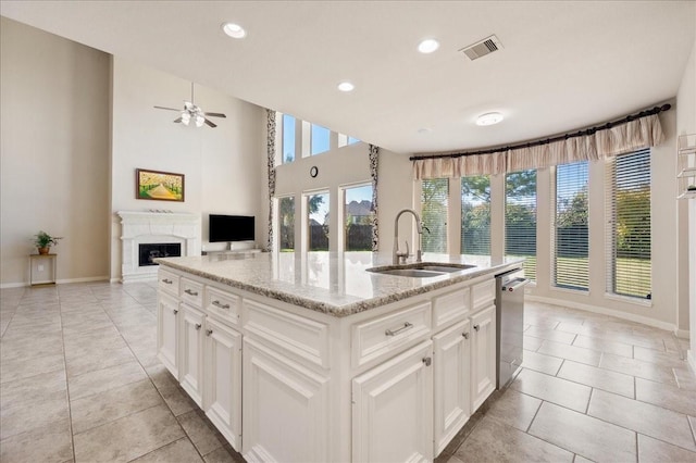 kitchen with sink, a kitchen island with sink, white cabinetry, light stone countertops, and light tile patterned flooring