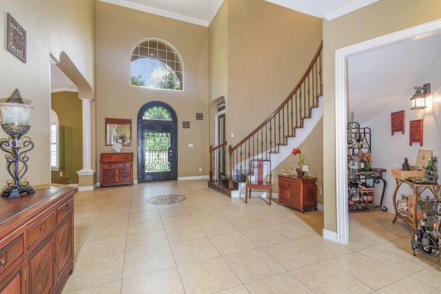 entryway featuring crown molding, a towering ceiling, decorative columns, and light tile patterned floors