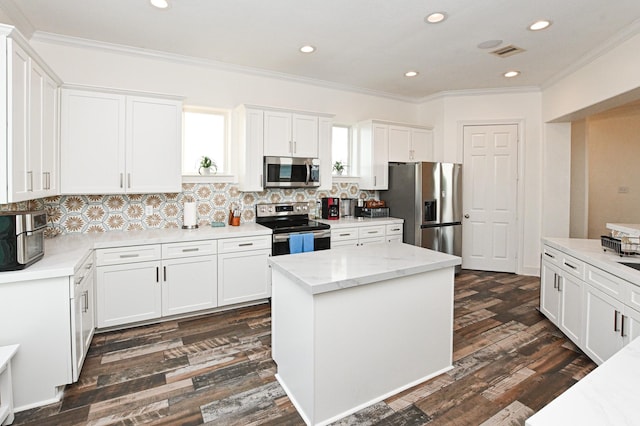 kitchen with a kitchen island, white cabinetry, light stone counters, stainless steel appliances, and crown molding