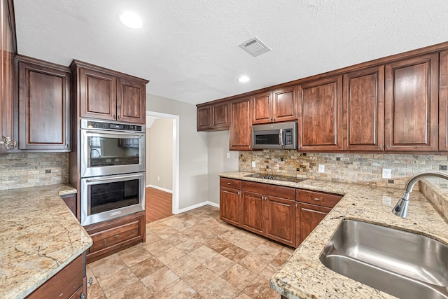 kitchen with light stone counters, sink, backsplash, and stainless steel appliances