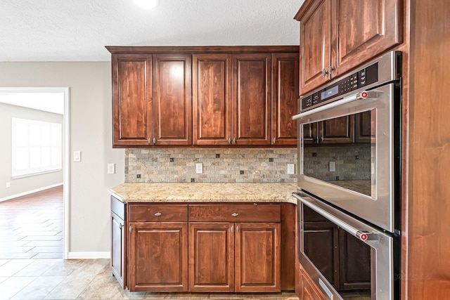 kitchen with light tile patterned flooring, decorative backsplash, light stone counters, stainless steel double oven, and a textured ceiling