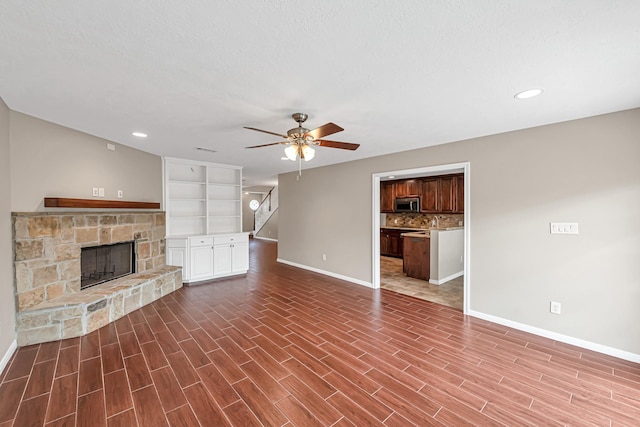 unfurnished living room with dark wood-type flooring, ceiling fan, a stone fireplace, and a textured ceiling