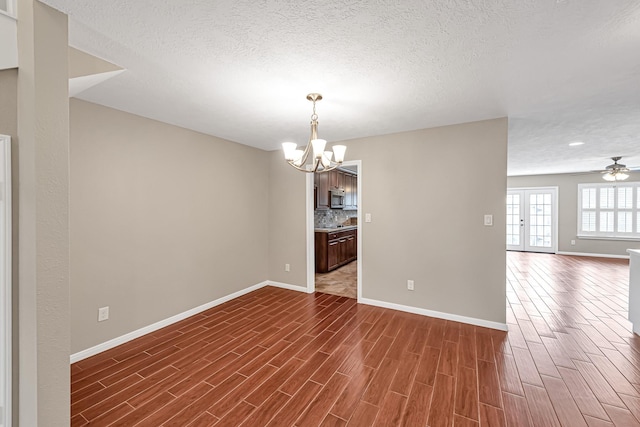 unfurnished room with french doors, dark hardwood / wood-style flooring, ceiling fan with notable chandelier, and a textured ceiling