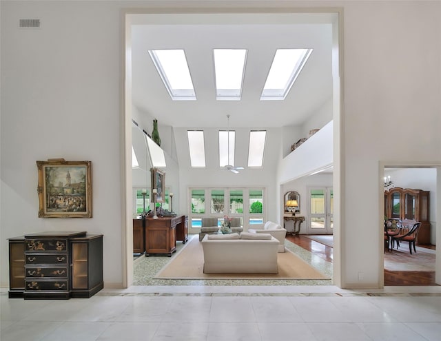 living area with a high ceiling, a skylight, visible vents, and tile patterned floors