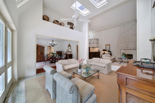 living area featuring high vaulted ceiling, a skylight, a large fireplace, and ceiling fan with notable chandelier