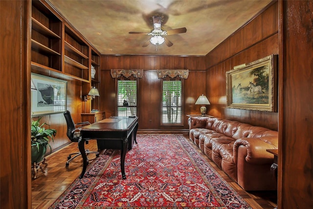 office space with built in shelves, ceiling fan, and wooden walls