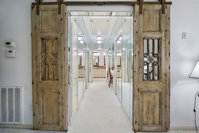 corridor with a barn door, visible vents, and light colored carpet