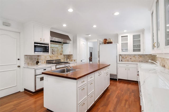 kitchen featuring a center island with sink, gas range, stainless steel microwave, wall chimney range hood, and a sink