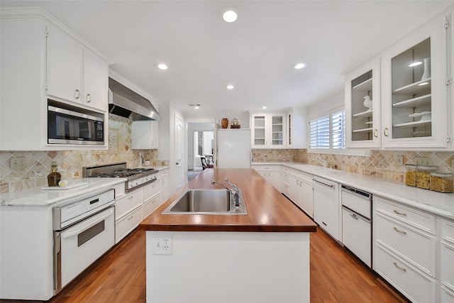 kitchen with white appliances, a kitchen island with sink, a sink, and wall chimney range hood