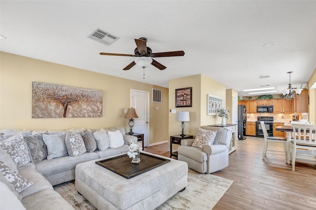 living room with visible vents, ceiling fan with notable chandelier, baseboards, and light wood finished floors