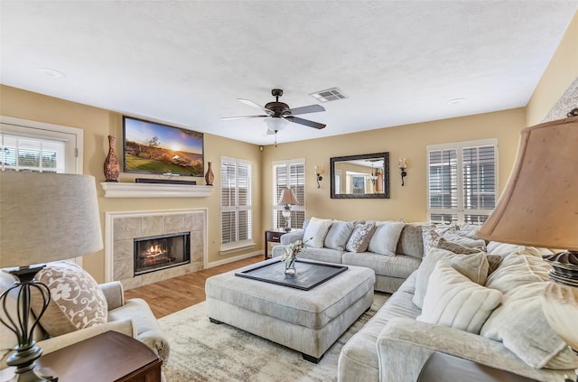 living area featuring visible vents, a ceiling fan, wood finished floors, and a tiled fireplace