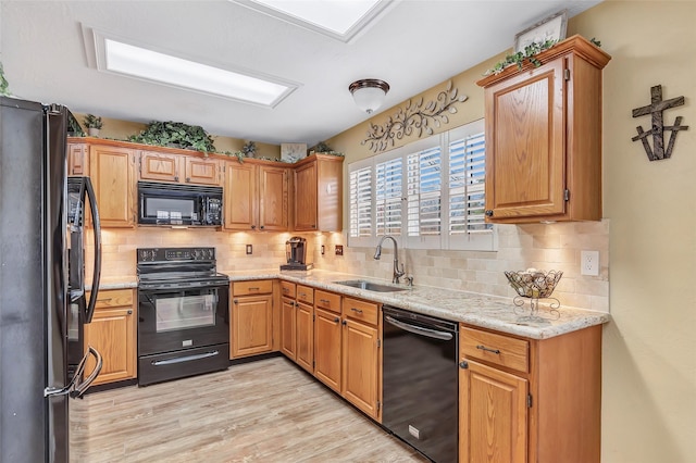 kitchen with light stone counters, a sink, black appliances, light wood-style floors, and backsplash