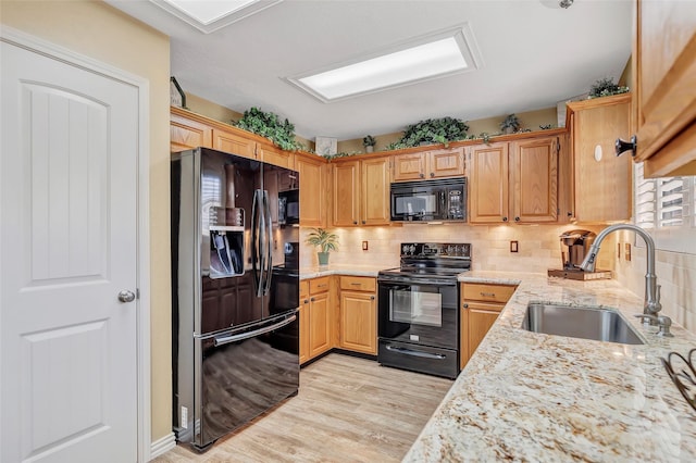 kitchen featuring light stone counters, a sink, decorative backsplash, black appliances, and light wood-type flooring