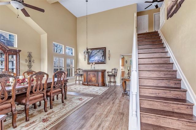 dining room with stairway, wood finished floors, a towering ceiling, and ceiling fan with notable chandelier