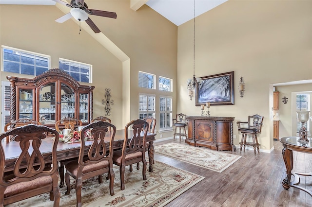 dining room featuring ceiling fan with notable chandelier, high vaulted ceiling, baseboards, and wood finished floors