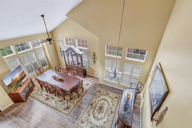 living area with ceiling fan with notable chandelier, wood finished floors, baseboards, and high vaulted ceiling