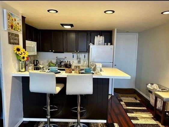 kitchen featuring white appliances, a kitchen breakfast bar, and kitchen peninsula