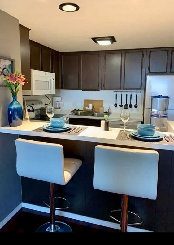 kitchen with dark brown cabinetry, range, a breakfast bar, and sink