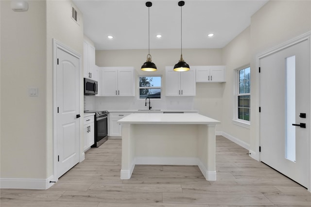 kitchen featuring a kitchen island, appliances with stainless steel finishes, decorative light fixtures, white cabinetry, and light hardwood / wood-style floors