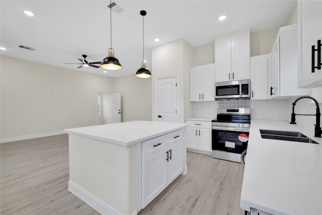 kitchen with sink, a center island, light wood-type flooring, appliances with stainless steel finishes, and white cabinets